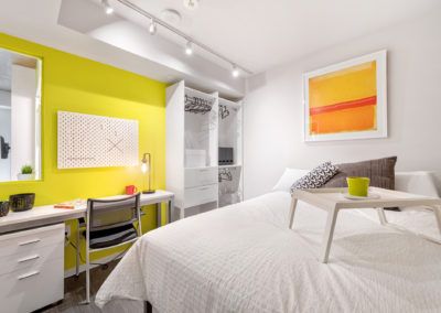 Modern apartment bedroom featuring white furniture with a bright yellow accent wall.